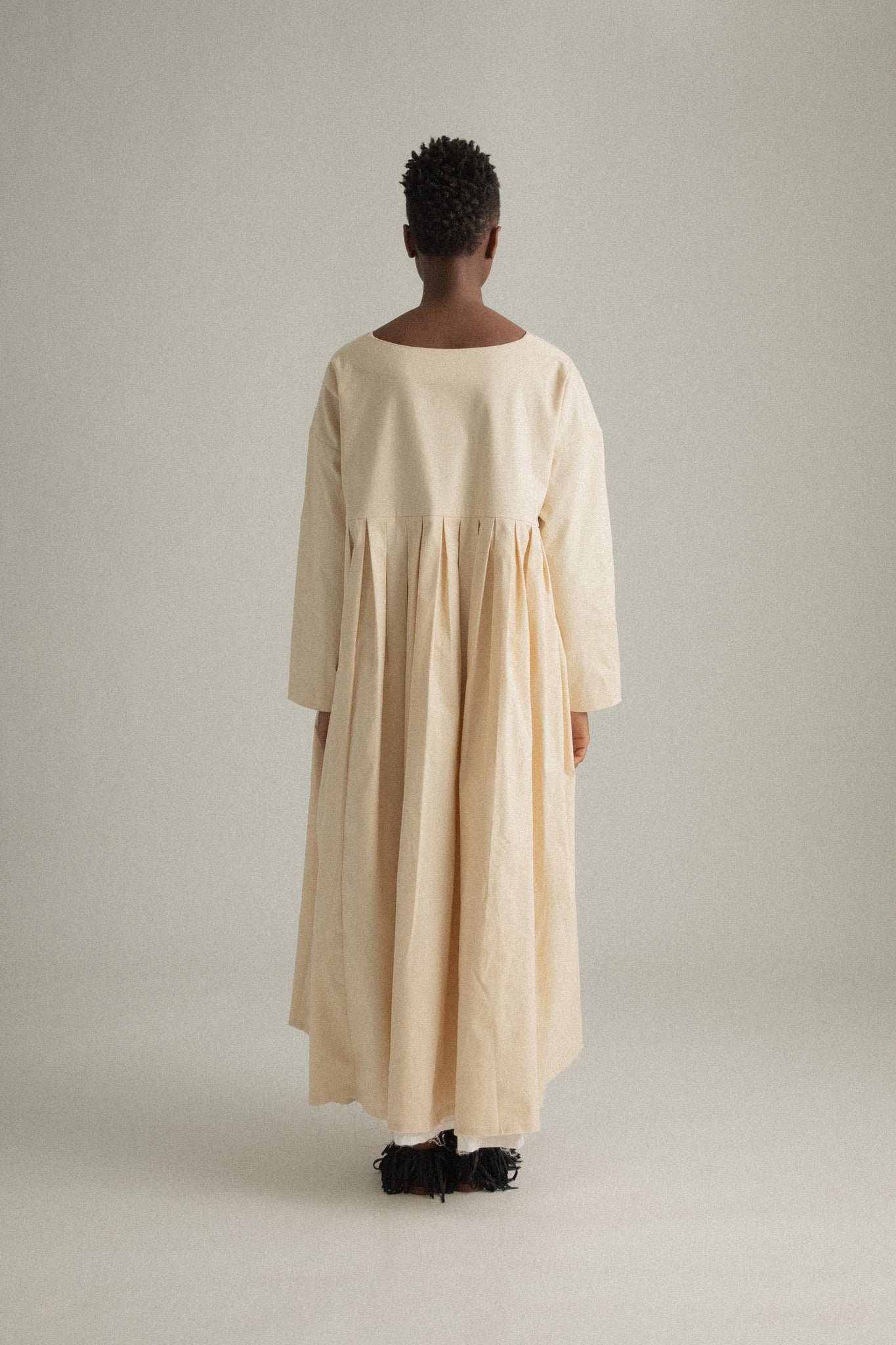  Back view of Arya Dress in compact cream cotton, showing the rounded neckline and gathered details.