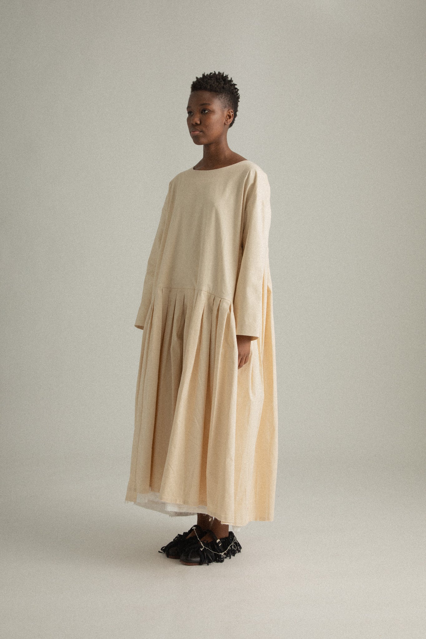 Side view of Arya Dress in compact cream cotton, emphasizing the pleated skirt and loose silhouette.