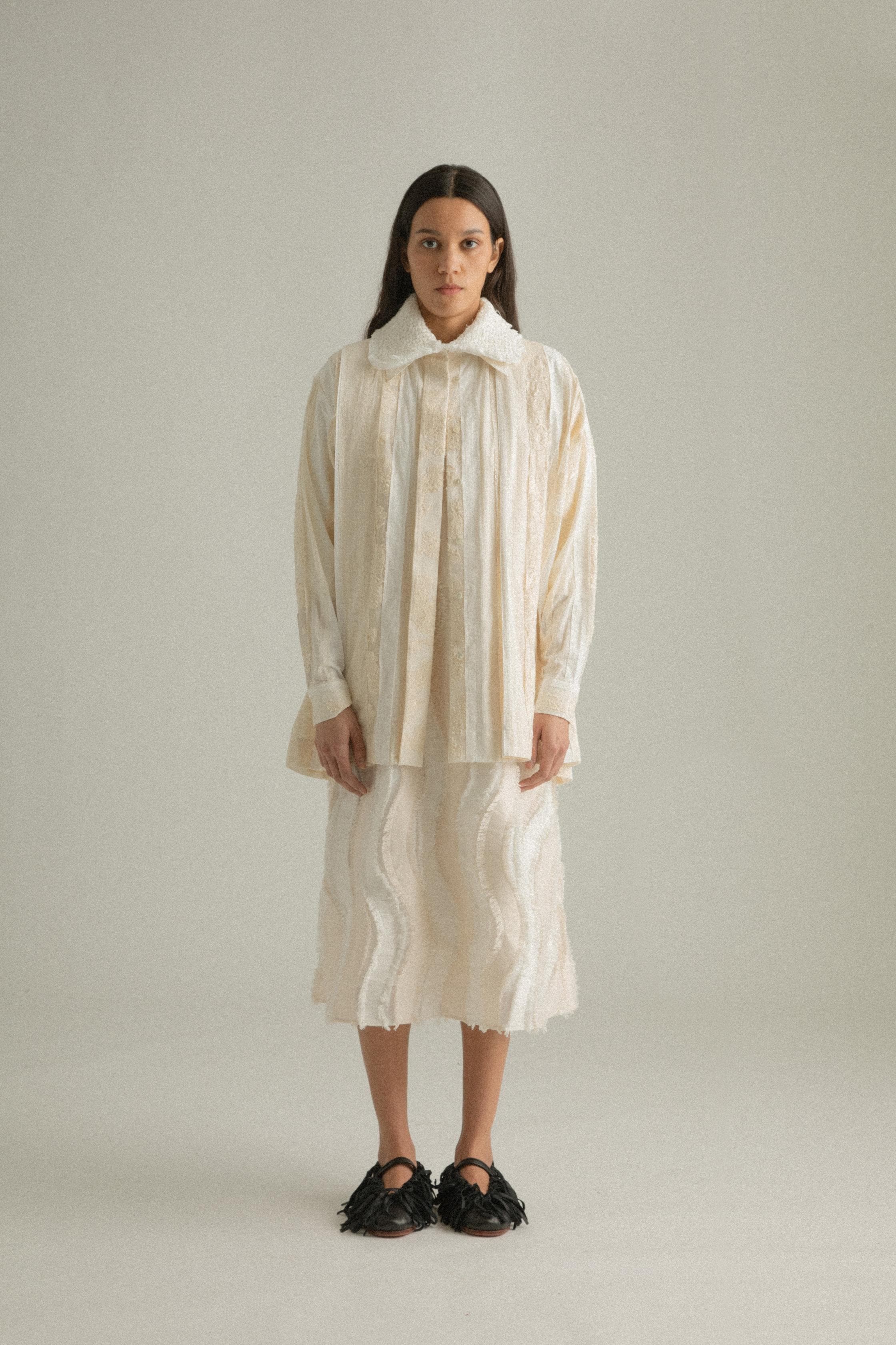 A model wearing the Bing Top, a blend of cotton, polyester, silk, and lyocell in natural tones. The top has a structured front with subtle pleating and a back-tied design, styled over the Lena Dress. The model is shown in front, side, and back views to showcase the top’s texture and fit