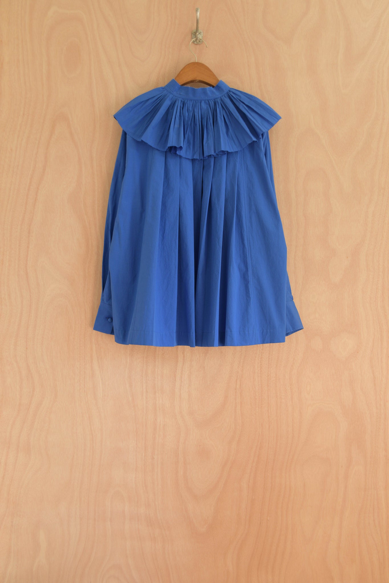 Back view of Carcy Top in blue, showcasing flowing pleats.