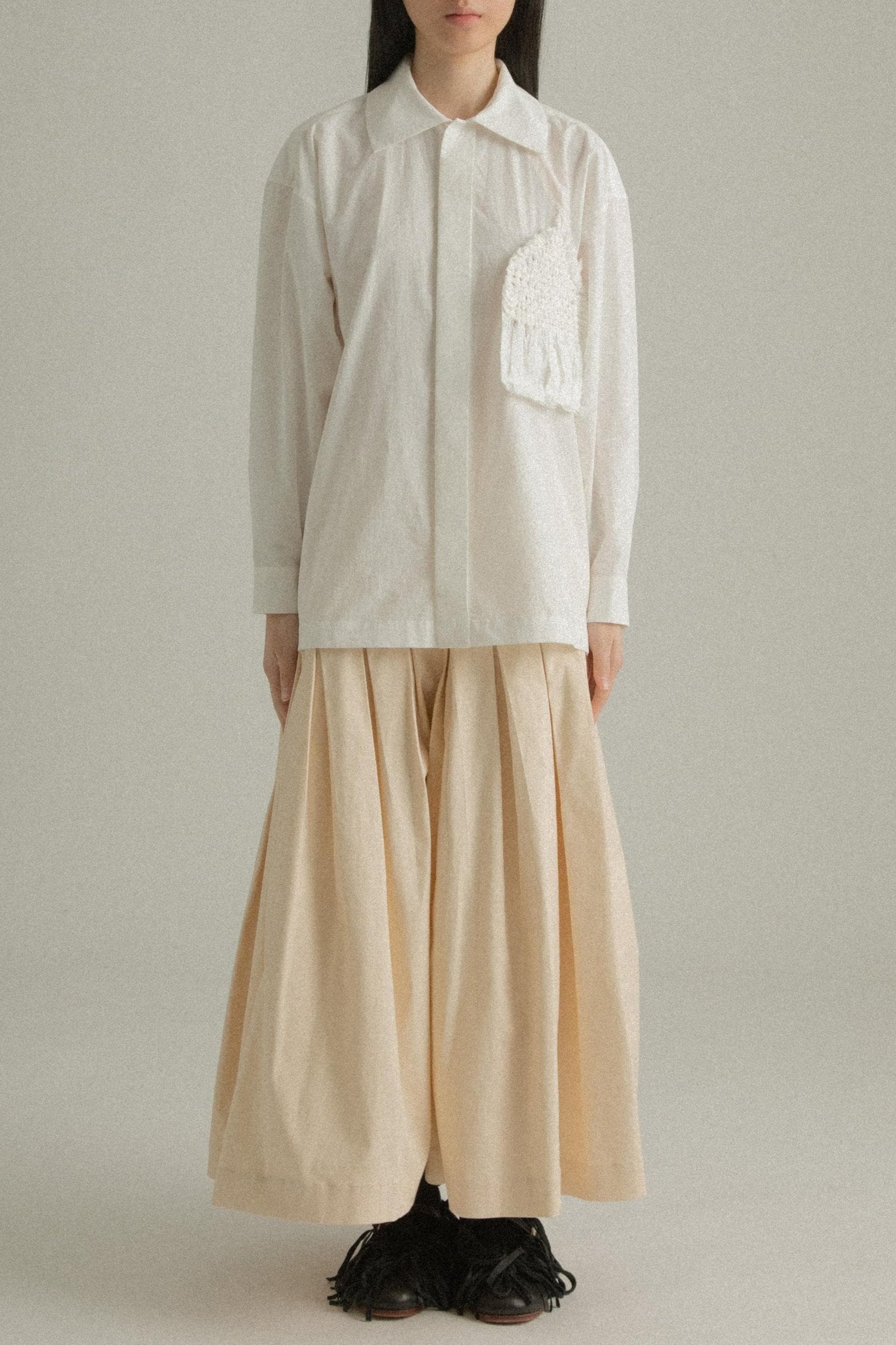 A model wearing the Charlotte Shirt, made from 100% organic cotton with intricate hand-knit detailing on the chest pocket. The shirt is paired with the Clara Skirt, presenting a balanced and fluid ensemble. The model is shown in front, side, and back views to showcase the shirt’s relaxed fit and unique design elements.