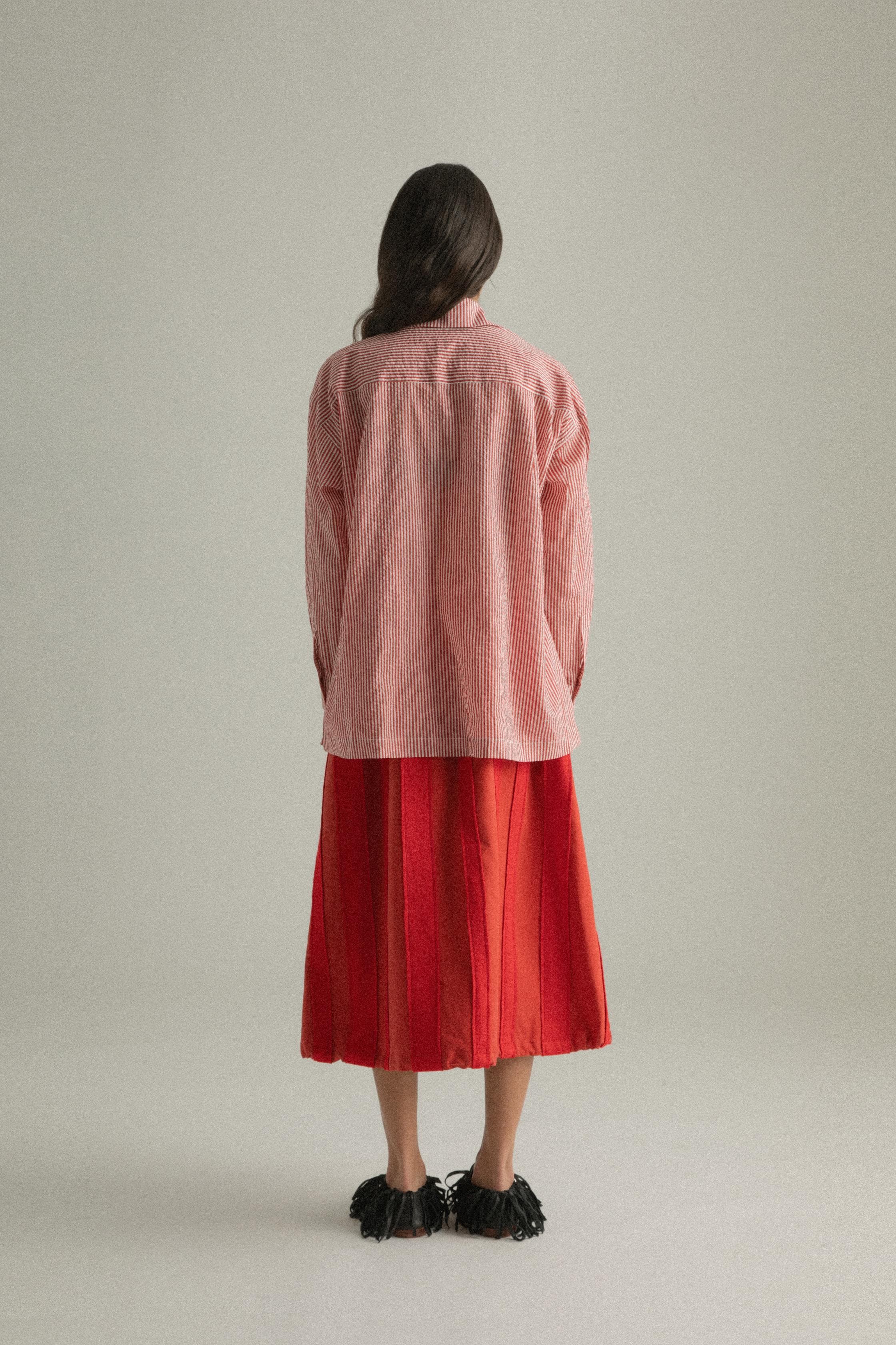 A model wearing the Charlotte Shirt, made from 100% organic cotton with woven stripes and a hand-knit detailed chest pocket. The shirt is styled with the Lulu Skirt, presenting a cohesive look. The model is shown in front, side, and back views to showcase the shirt’s relaxed fit and design elements.