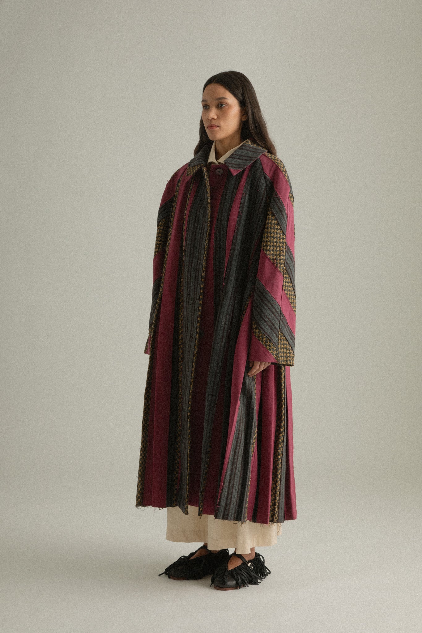 Side view of Emmeline Coat, highlighting multi-fabric patchwork and draped silhouette.