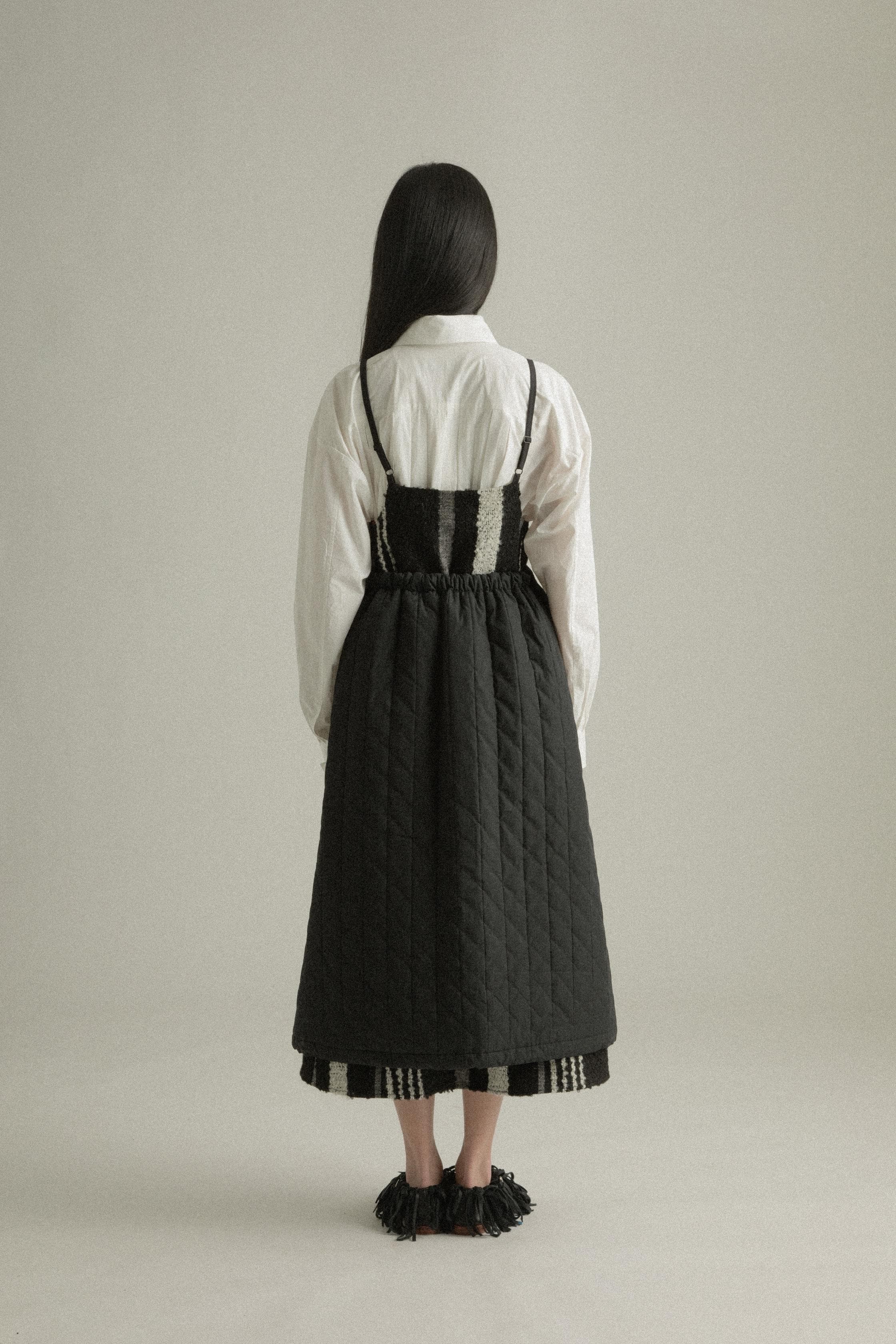 A model wearing the Lulu Skirt, crafted from 100% organic cotton with a quilted texture. The skirt features an A-line silhouette and is layered over the Lena Dress, adding dimension and warmth. The model is shown in front, side, and back views.