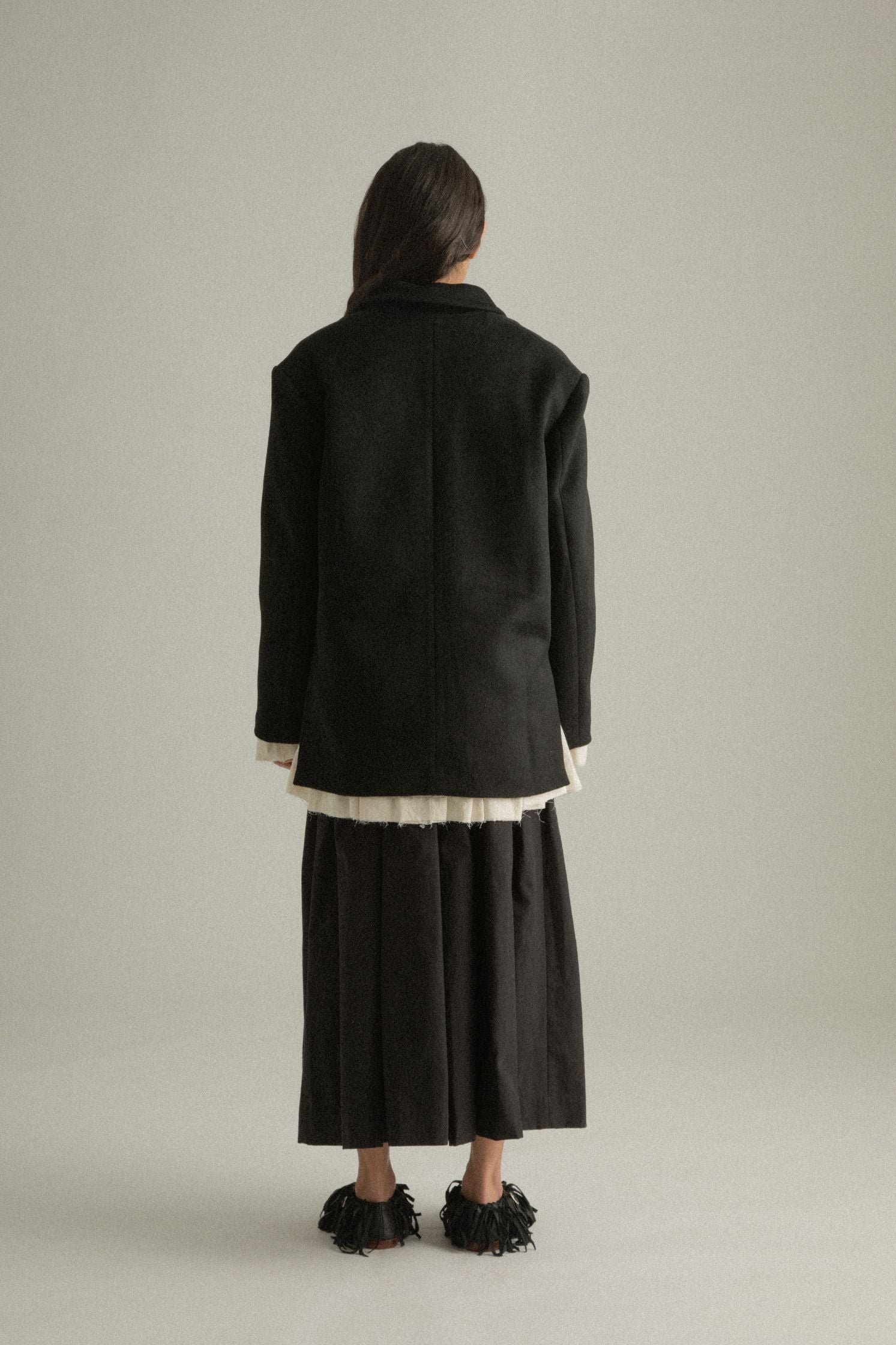 Back view of the Martha Coat on the black wool side, emphasizing pleating details and clean structure.