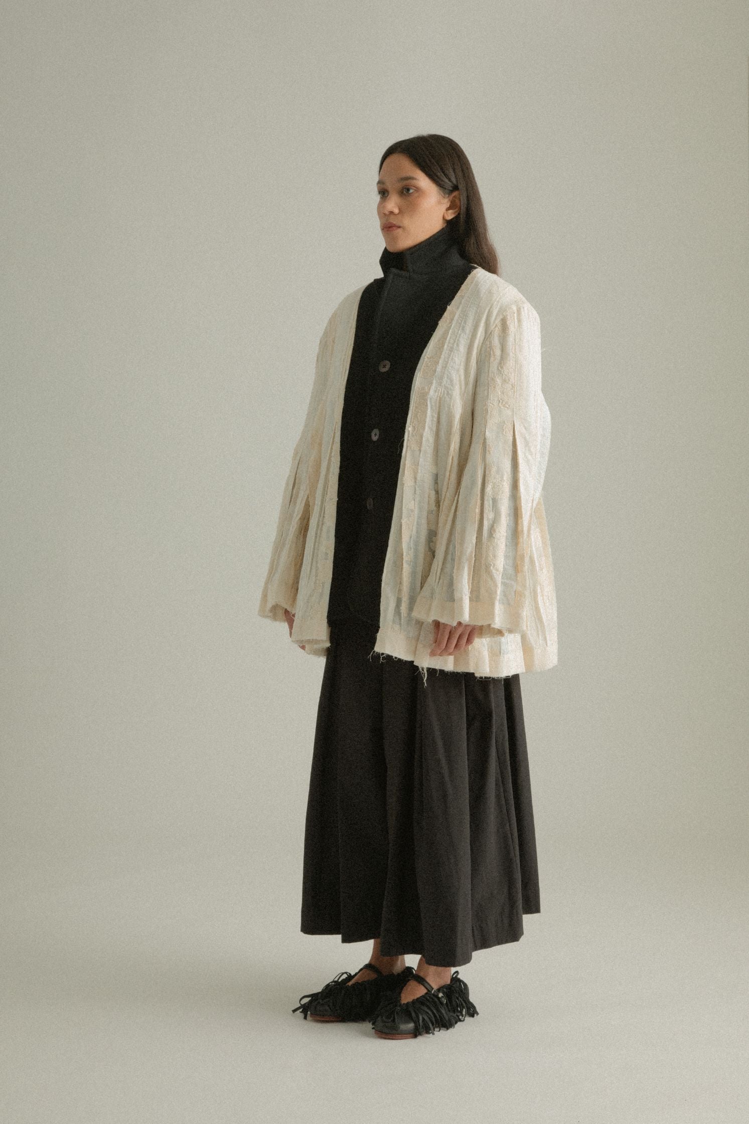 Side view of the Martha Coat’s cream patchwork side, emphasizing its artisanal textures and pleats.