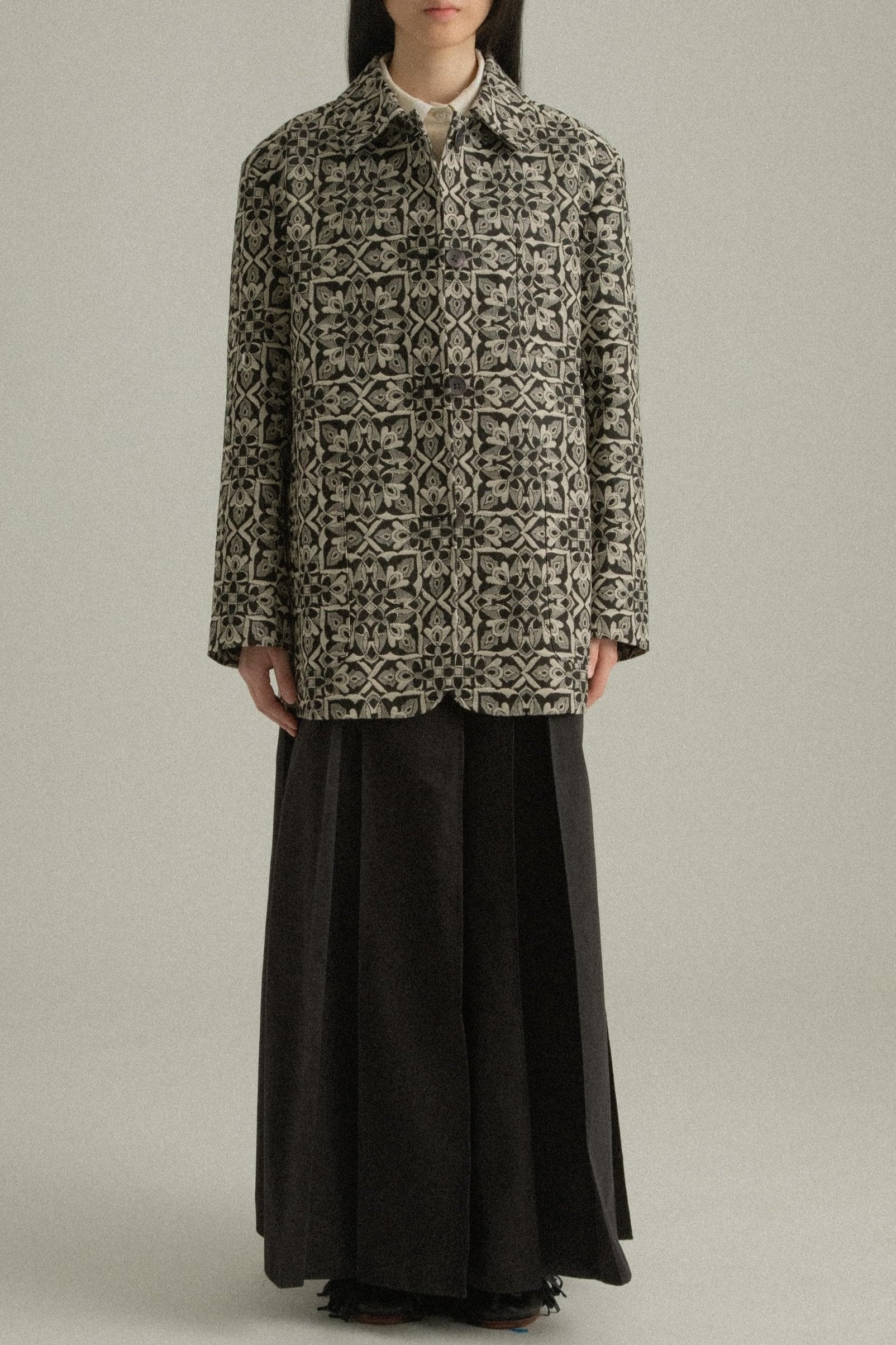 A model wearing the Nicole Jacket, featuring a classic round collar and single-button closure. Crafted from a cotton-lyocell blend with an intricate jacquard pattern inspired by mountain flora. Styled with the Rayna Pants for a balanced, textured look. The model is shown in front, side, and back views.