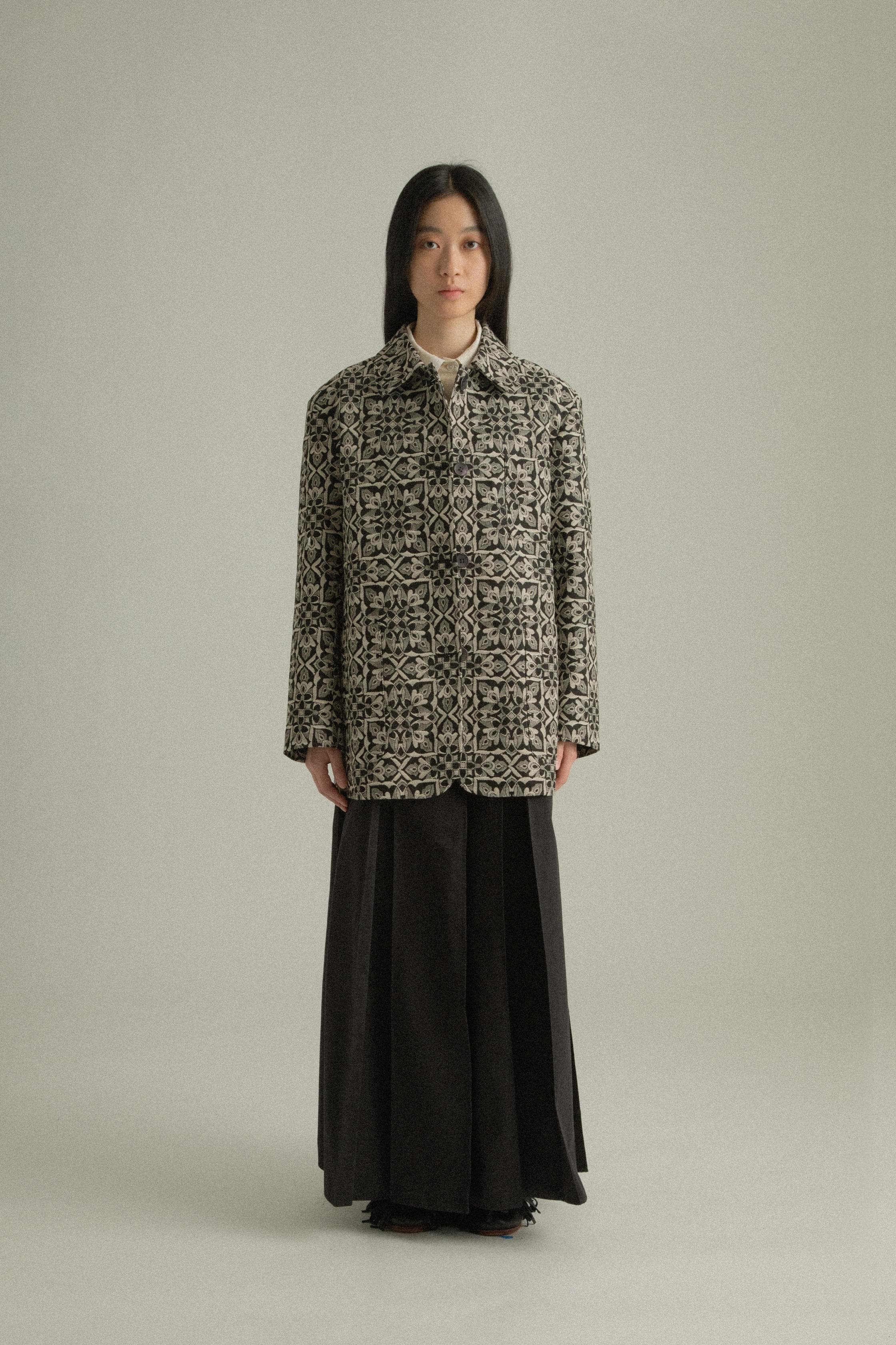 A model wearing the Nicole Jacket, featuring a classic round collar and single-button closure. Crafted from a cotton-lyocell blend with an intricate jacquard pattern inspired by mountain flora. Styled with the Rayna Pants for a balanced, textured look. The model is shown in front, side, and back views.