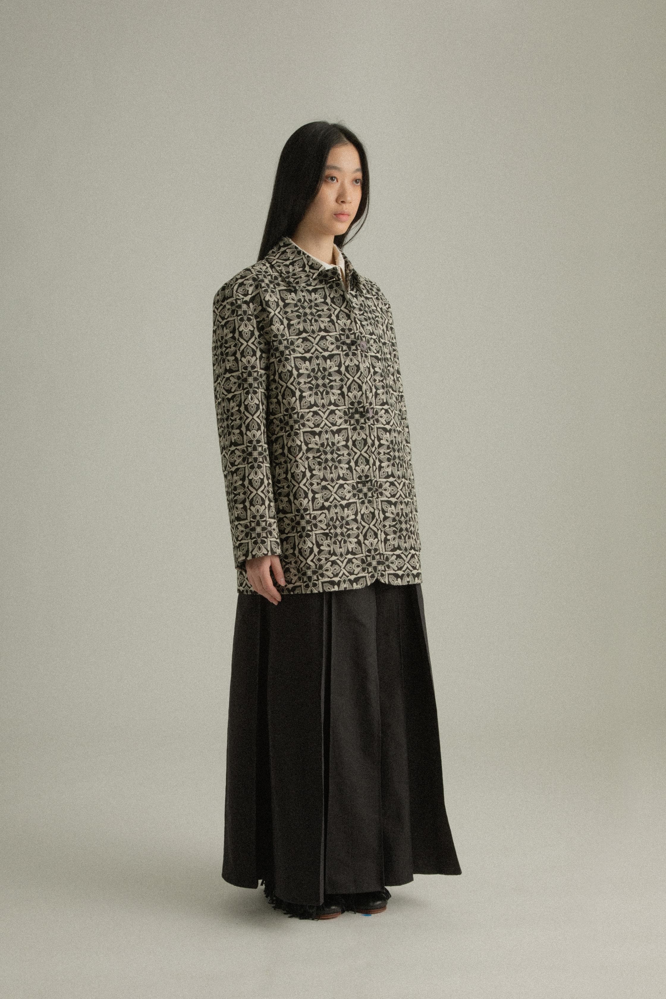 A model wearing the Nicole Jacket, featuring a classic round collar and single-button closure. Crafted from a cotton-lyocell blend with an intricate jacquard pattern inspired by mountain flora. Styled with the Rayna Pants for a balanced, textured look. The model is shown in front, side, and back views.